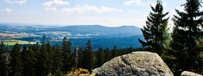 Ein Aussichtsbild von einem Berg mit Blick auf einen Wald mit Nadelbäumen und Dorfflächen im Fichtelgebirge als Beispielziel für einen Sommerurlaub in Bayern.