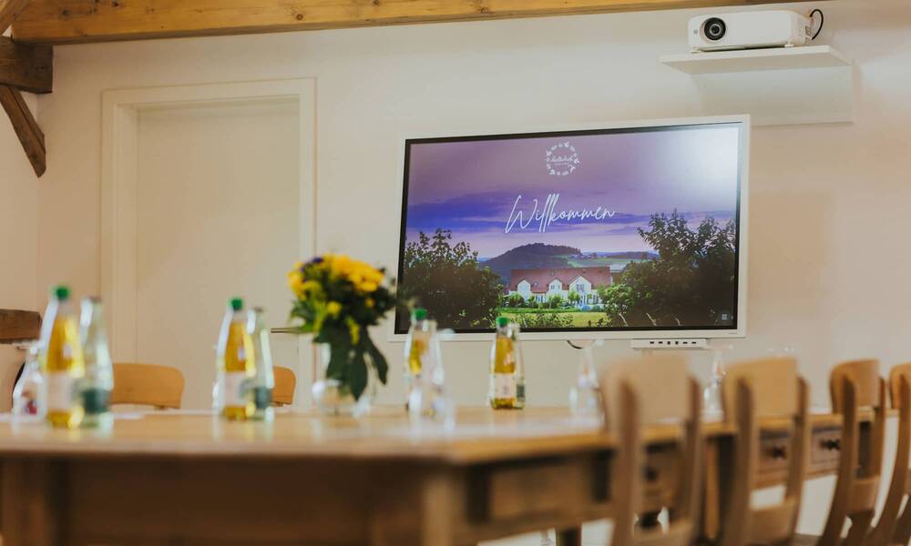 Meeting room with wooden chairs, apple spritzer and water as drinks on the table and modern presentation screen displaying a ‘Welcome’ sign, ideal for meetings and seminars in a cosy atmosphere.