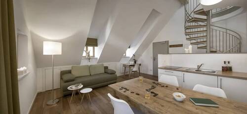 The living and dining room with kitchenette, rustic table, green sofa and spiral staircase to the gallery in one of the Hollerhöfe holiday homes.