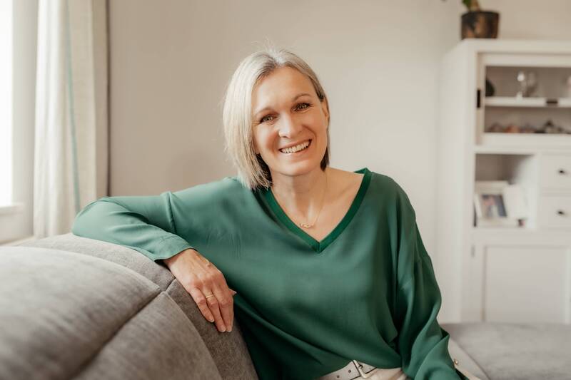 Doris Völkl sitzt lächelnd auf einem Sofa, Referentin des Business-Frühstücks in den Hollerhöfen zum Thema Kommunikation und Wirkung.