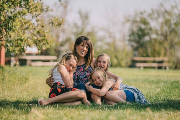 A mother sitting in a green meadow with her three daughters in her arms - an example of a holiday with the family.
