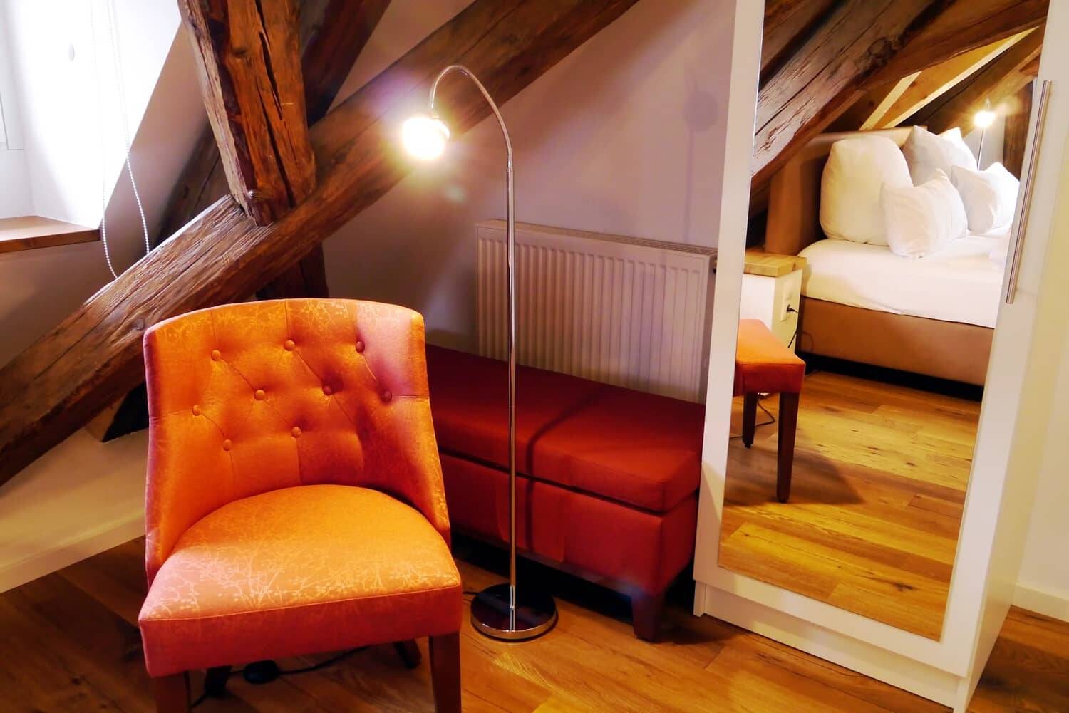 Ein oranger Sessel mit Leselampe und Spiegel im Doppelzimmer Superior.
