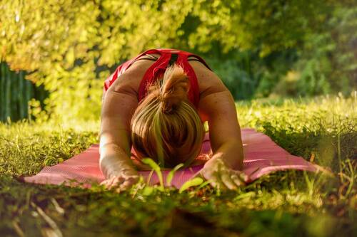 Woman in child's pose on a yoga mat in the countryside, surrounded by trees and warm sunlight - shows the natural tranquillity of the Hollerhöfe as a possible location for yoga retreats.