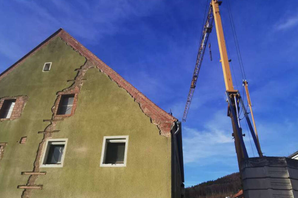 The front of a green house against a bright blue sky, with a crane visible next to it. The village house is currently being renovated for new Hollerhöfe holiday flats.