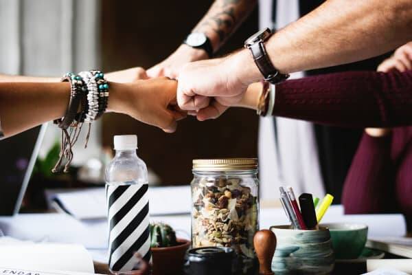 Hands of several people coming together for a symbolic "high-five" – an image that represents team building and team events in the summer, fostering collaboration and unity.