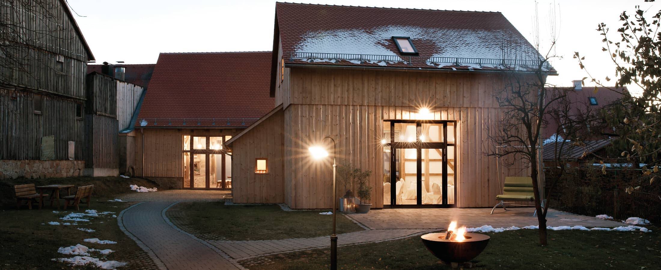 Die Hollerscheune von außen in der Abenddämmerung fotografiert, innen hell beleuchtet und mit leichtem Schneezucker auf dem Dach – eine ideale Location für stimmungsvolle Weihnachtsfeiern..