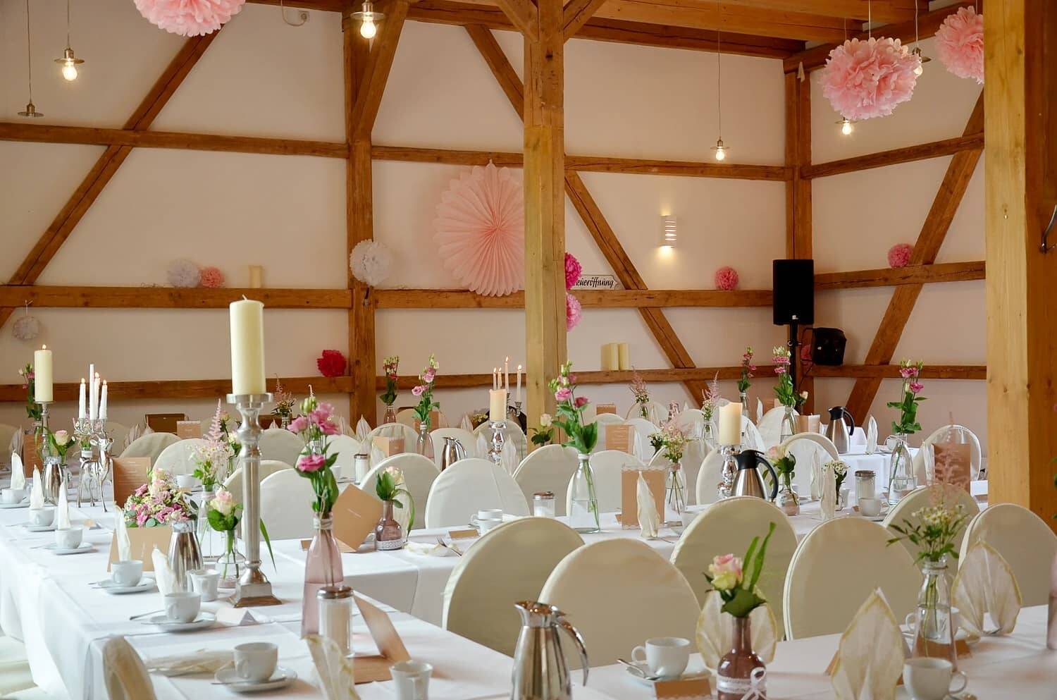 Eine große Festtafel in der Hollerscheune, festlich eingedeckt und mit blumiger, rosa Dekoration.