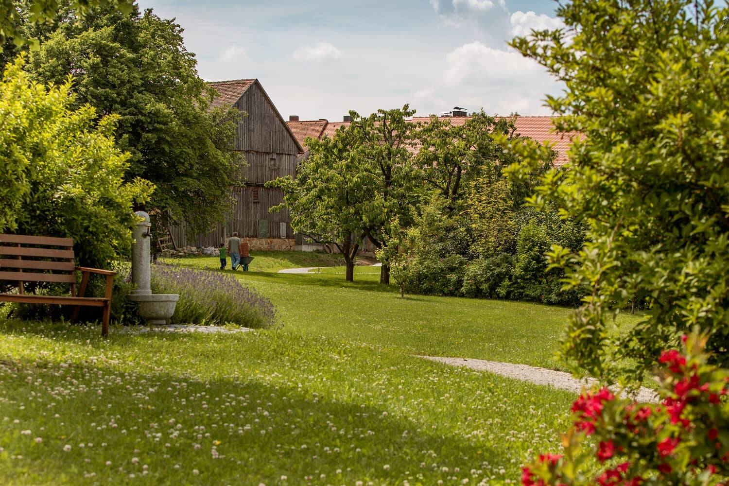 The idyllic garden of the Naturhotel Hollerhöfe with its well-tended lawn, lined with trees and flowering shrubs.