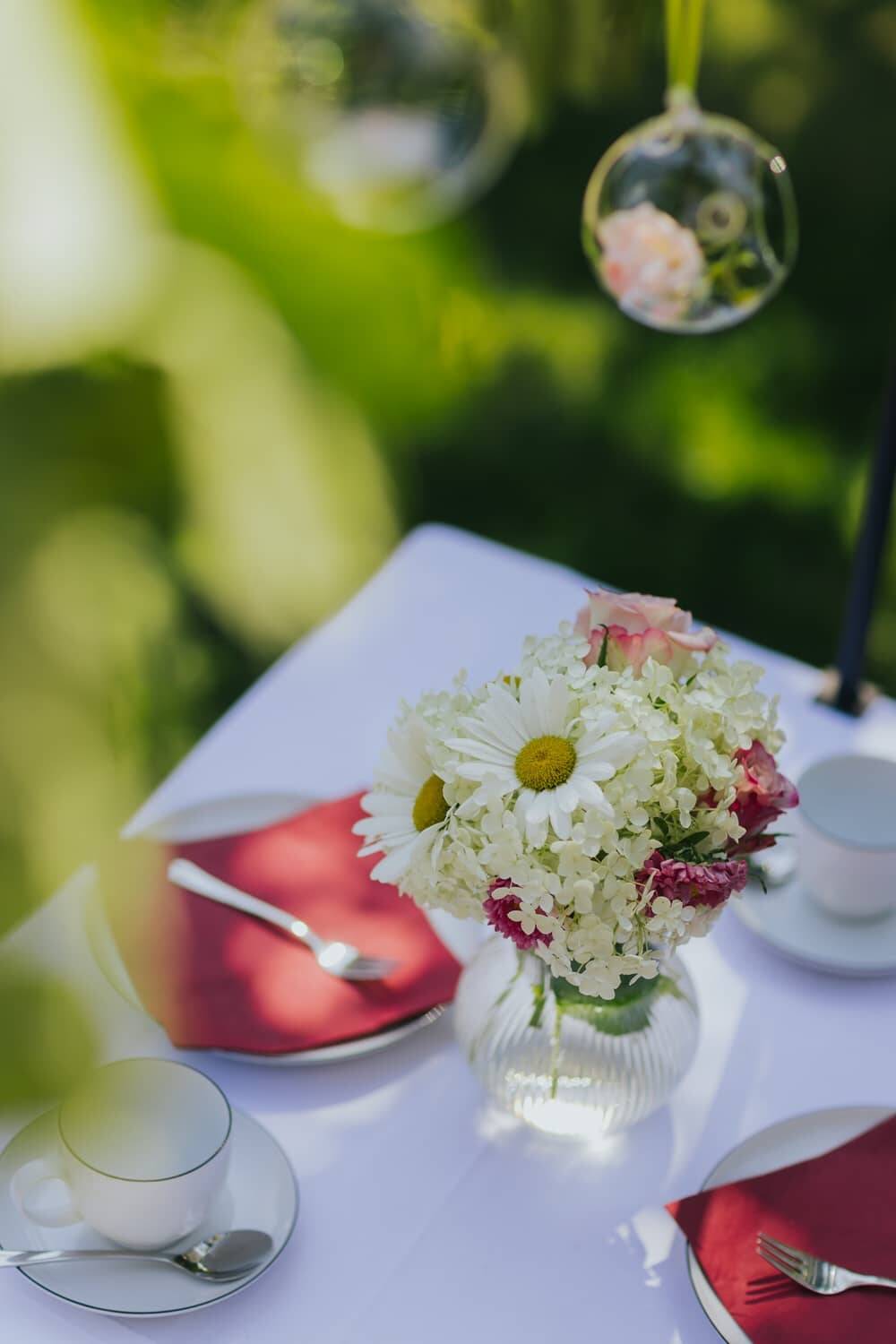 Festlich gedeckter Gartentisch mit Blumenstrauß und roten Servietten unter freiem Himmel - eine herrliche Location zum Draußen-Feiern.