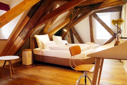 The bedroom in the Kösslerhaus, with high ceilings, wooden beams and a small desk.