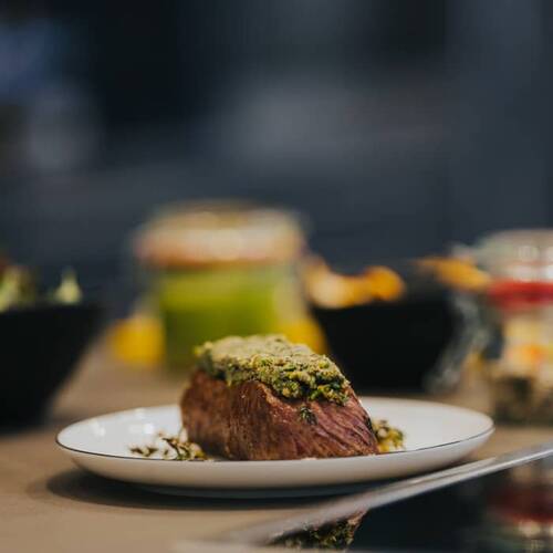Zartes Stück Fleisch mit Kräuterkruste auf einem weißen Teller, begleitet von stilvoll angerichteten Beilagen – feine Kulinarik in den Hollerhöfen, einer Eventlocation mit Catering.