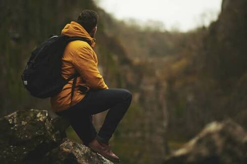 Ein Wanderer in einer senfgelben Jacke sitzt auf einem Felsen und blickt mit dem Gesicht weggedreht auf die weitläufige Landschaft – ein Beispielbild für Wanderungen in der Oberpfalz, die tolle Naturerlebnisse bieten.