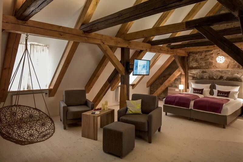 Das große Zimmer in dem Hotel in Kemnath zeigt einen großen Wohn- und Schlafraum mit Sitzlounge, Hängesessel und Bett. Die Einrichtung ist rustikal mit Natursteinen in der Wand und Deckenbalken aus Holz.