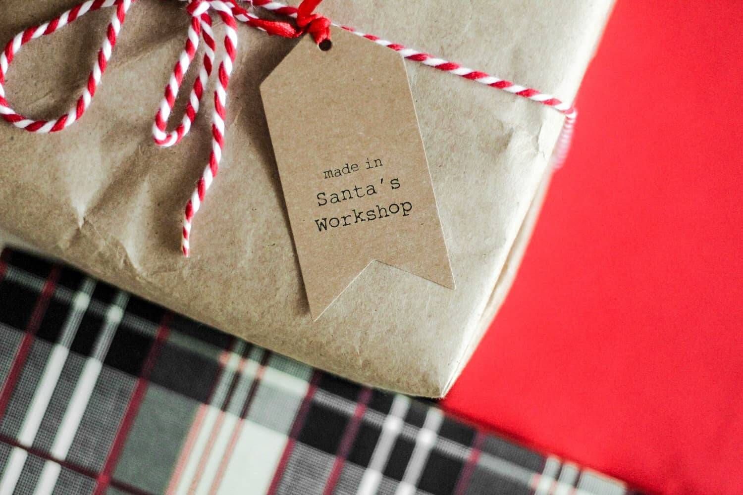 Geschenk verpackt in braunem Papier mit einer "Made in Santa's Workshop"-Marke, umgeben von weihnachtlich gemustertem Papier – ein kreativer Hinweis auf Tipps für lustige Weihnachtsfeiern und originelle Geschenkideen.
