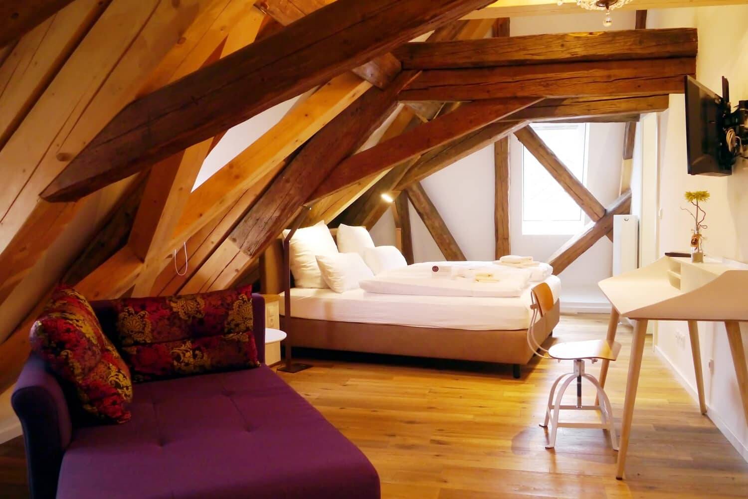 Das großräumige Doppelzimmer Superior mit Doppelbett, Schreibtisch, Fernseher und Sofa. Die rustikale Einrichtung mit den massiven Deckenbalken aus Holz zeigt die historische Anlehnung der Häuser.