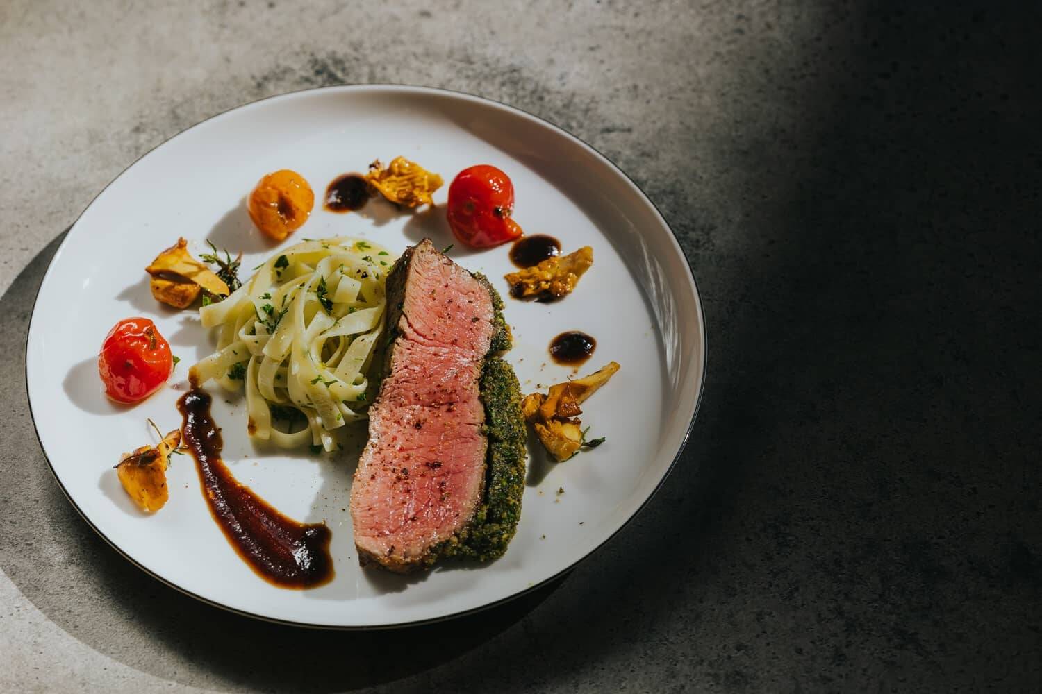 Fein angerichtetes Gericht mit rosa gebratenem Fleisch, Tagliatelle und Cherrytomaten als Beispielbild für die nachhaltige Küche in unserer Eventlocation.