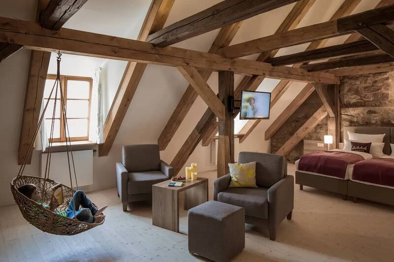 Das große Zimmer in dem Dorfhaus in Kemnath zeigt einen großen Wohn- und Schlafraum mit Sitzlounge, Hängesessel und Bett. Die Einrichtung ist rustikal mit Natursteinen in der Wand und Deckenbalken aus Holz.