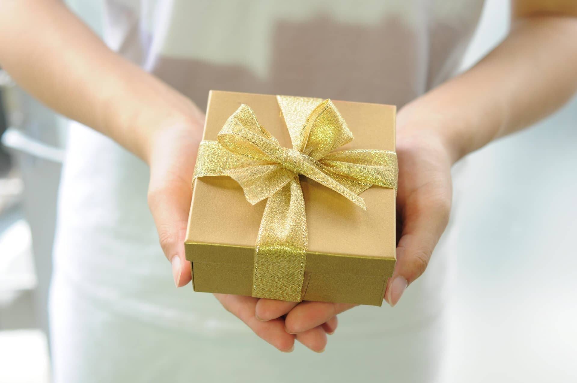 Person hält ein liebevoll verpacktes Geschenk mit goldener Schleife – ideal als Gutschein für eine Auszeit im Hotel im Grünen.