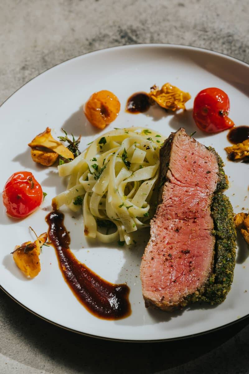 Eine Detailaufnahme eines rosa gebratenem Rinderfilets mit Tagliatelle als Beilage und angerichtet mit Gemüse als Sinnbild für die nachhaltige Küche in den Hollerhöfen.