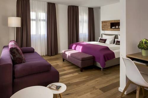 A bedroom and living room with double bed and purple sofa in one of the Hollerhöfe holiday homes.