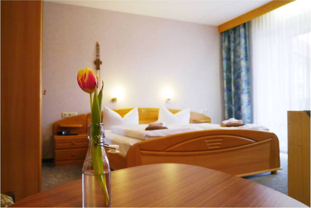 A double room in the Landgathof Zum Hirschen with a view of the bed, in the foreground a bottle with a red and yellow tulip in the centre.