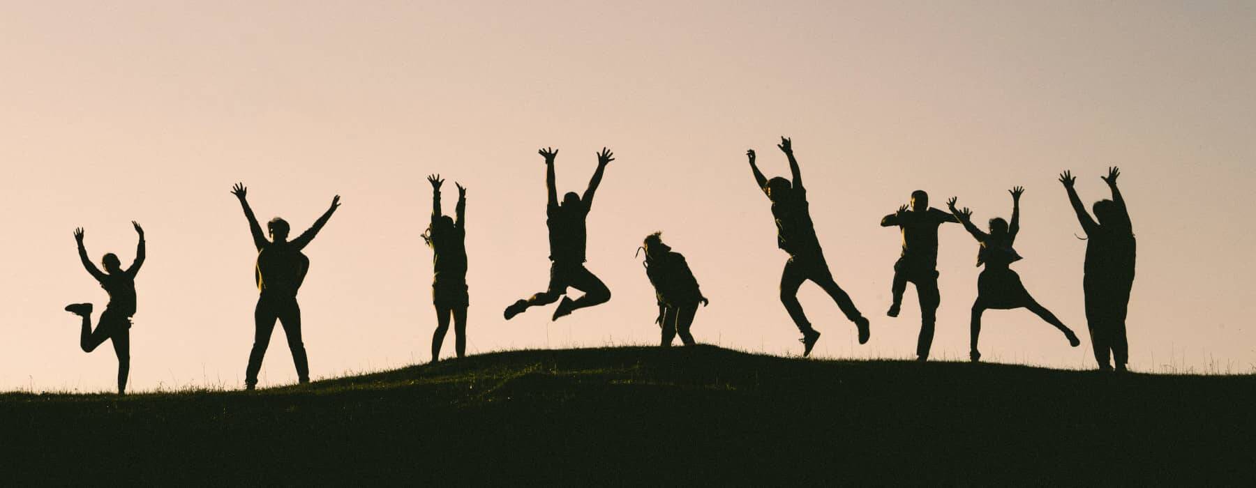 Silhouetten von neun Menschen in einer Reihe, die in die Luft springen – ein Beispielbild für Teamevents im Sommer.