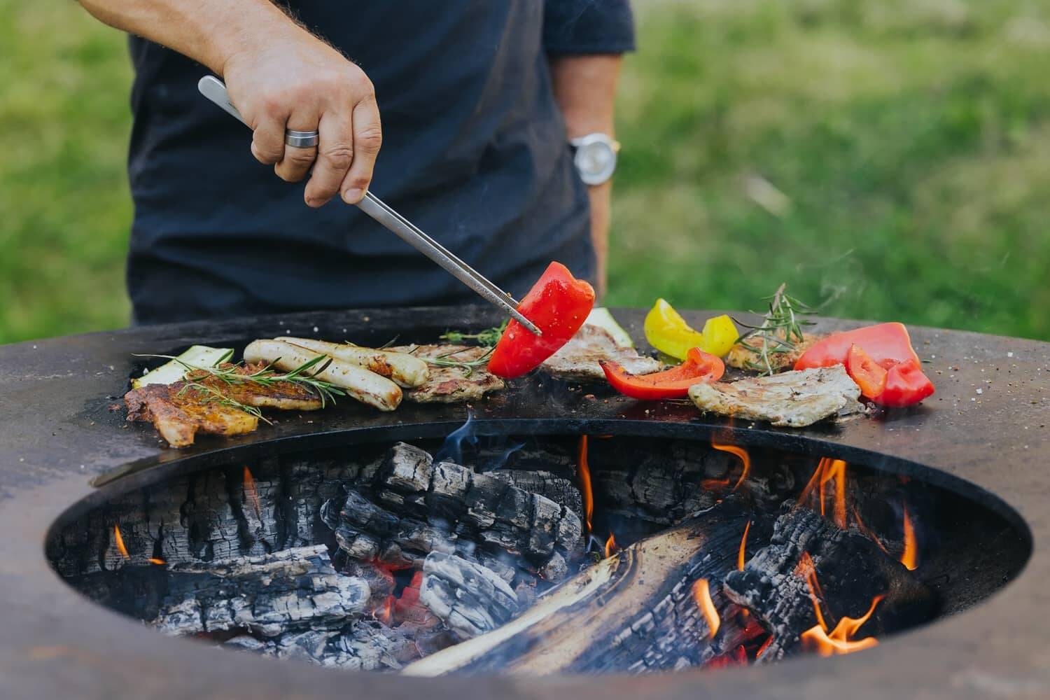 Person grillt buntes Gemüse und Fleisch über offenem Feuer auf einer Feuerschale – ideal für gesellige Runden in den Hollerhöfen als Eventlocation mit Grill.