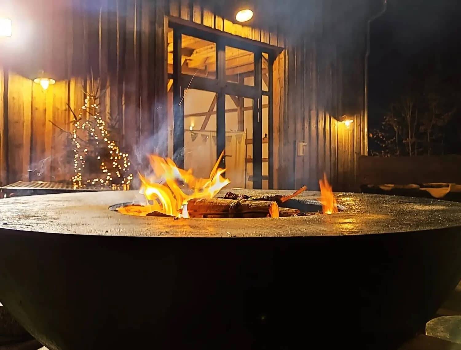 Gemütliches Lagerfeuer in einer Feuerschale vor der Hollerscheune als Weihnachtsfeier Location mit Grill.