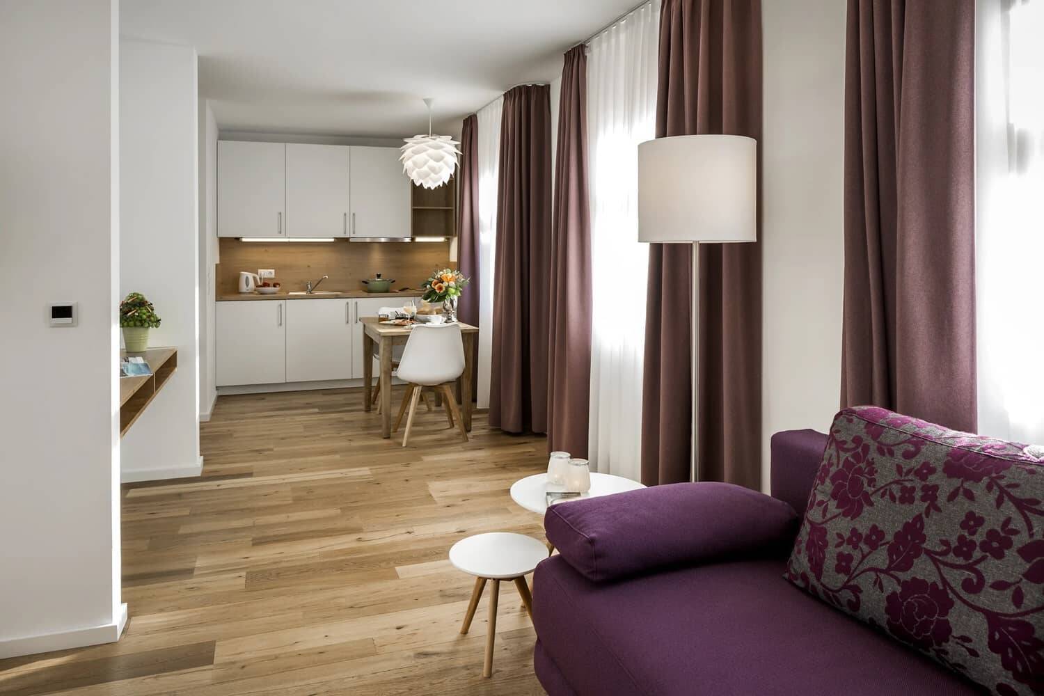 Der Wohnraum im 1-Raum-Apartment der Hollerhöfe mit Küchenzeile, kleinem Esstisch und Sofa mit Beistelltischchen.