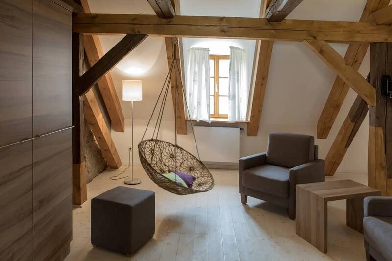 EIne Sitzlounge mit zwei Sesseln und einem geflochtenem Hängestuhl, der von den rustikalen Deckenbalken hängt.