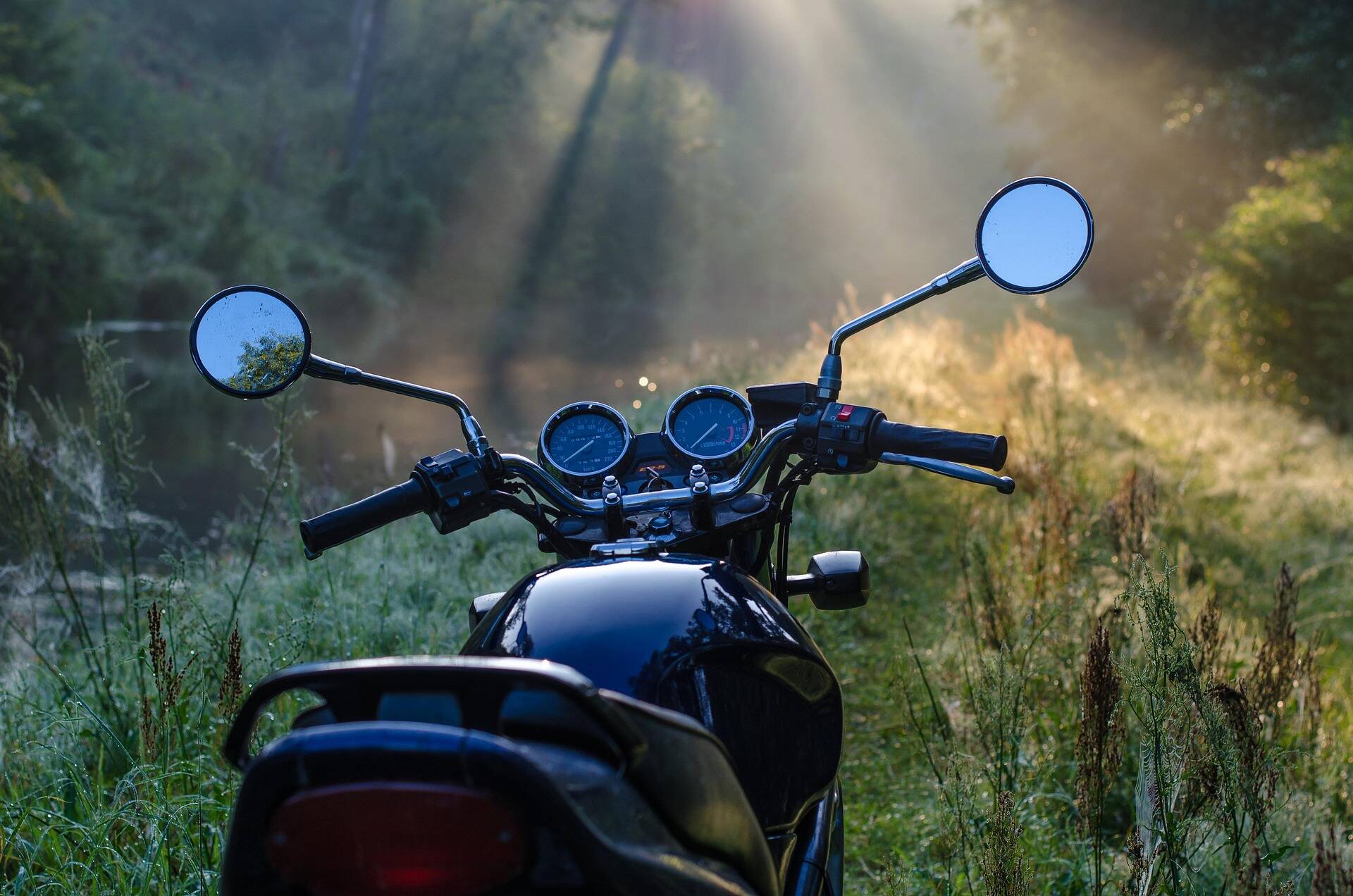 A black motorcycle stands amidst a green hilly landscape on a sunny day – a perfect scene for a motorcycle vacation in the Upper Palatinate.
