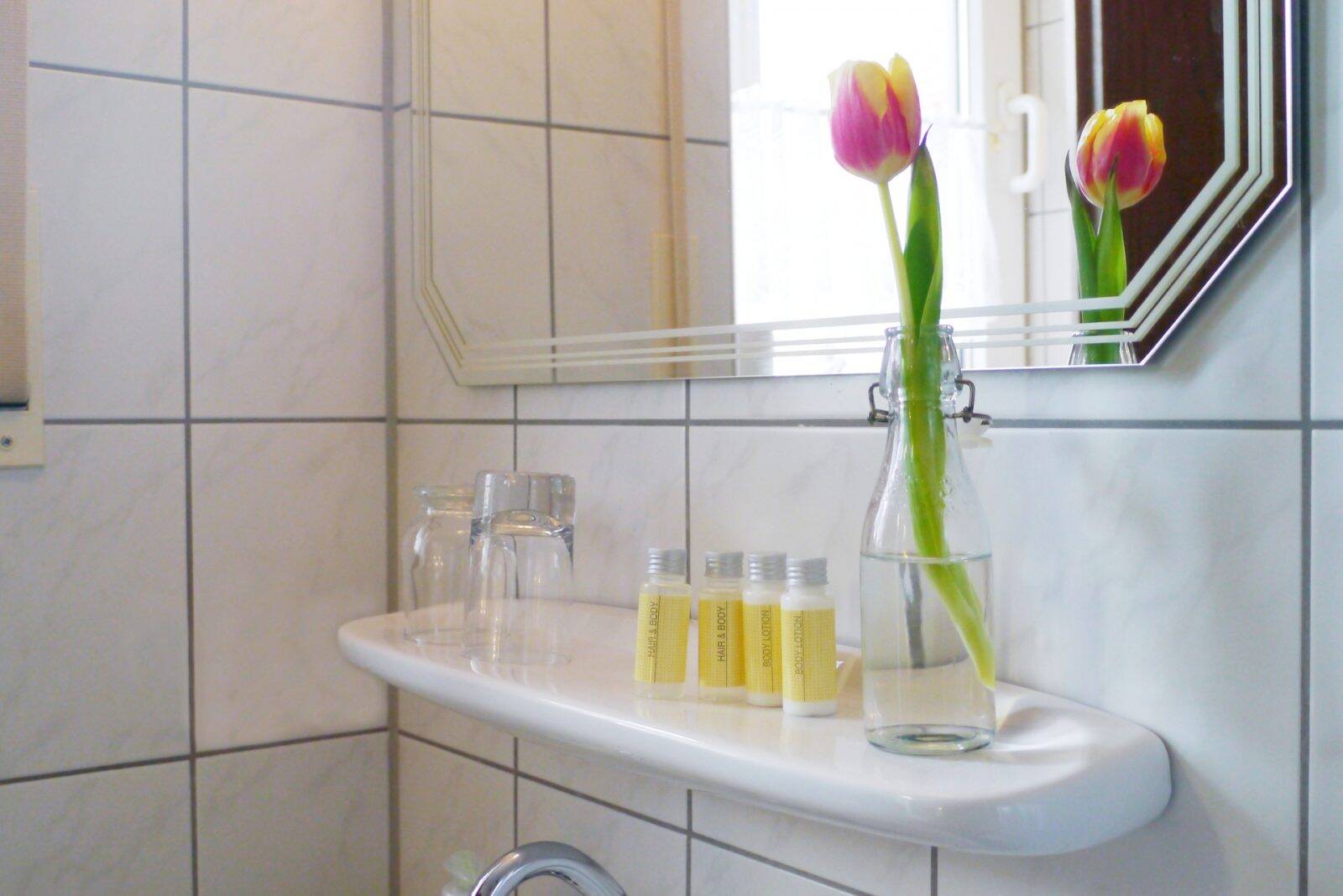 Eine Detailaufnahme des Badezimmerspiegels mit einer Tulpe zur Deko und den verschiedenen Kosmetikartikeln im Gasthof.
