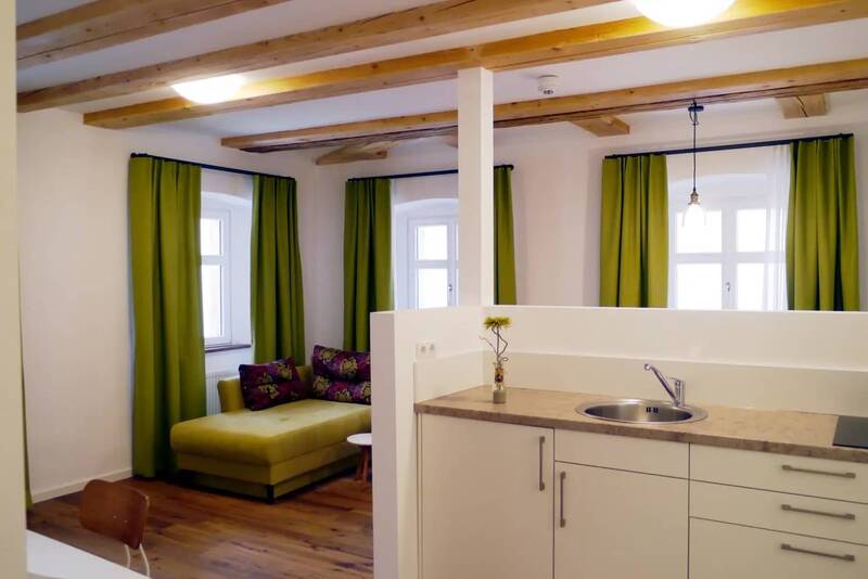 The living and dining area in the Kösslerhaus with a view of the kitchenette and a green two-seater sofa in the corner behind it.