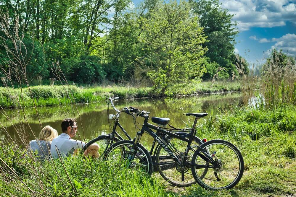 Two cyclists taking a break on an idyllic riverbank during their cycling holiday in the Upper Palatinate Forest.