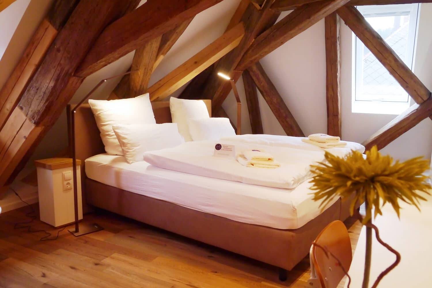 Ein Doppelbett mit rustikalen Deckenbalken in einem modernen Doppelzimmer der Hollerhöfe.
