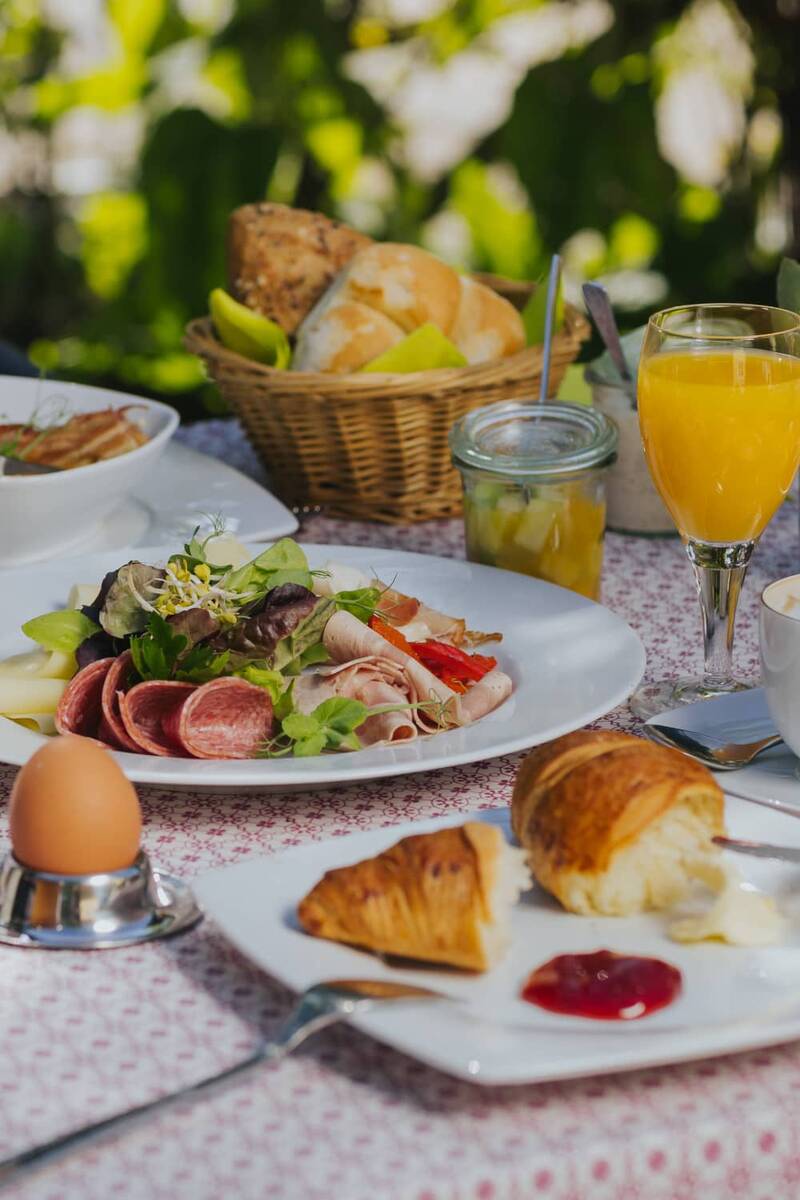Leckeres Frühstück mit frischen Brötchen, Aufschnitt, Salat, gekochtem Ei und Orangensaft – ein Beispiel für das Frühstücksangebot in unserem Hotel mit Ferienwohnungen in Bayern.